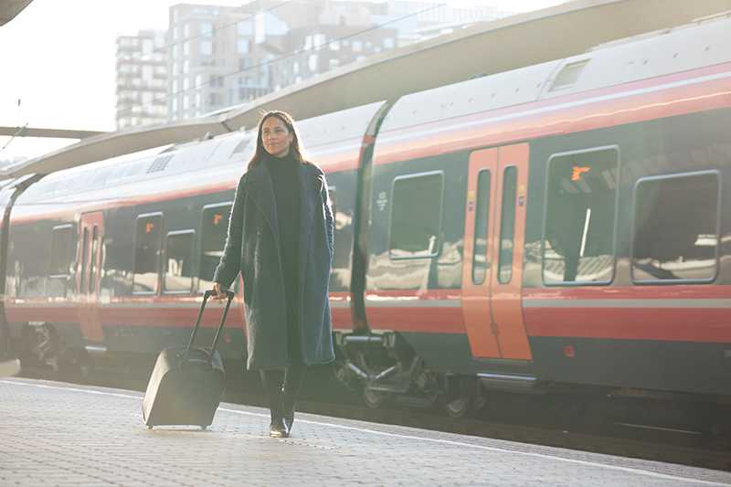 Kvinne med trillekoffert foran rødt tog på jernbanestasjon